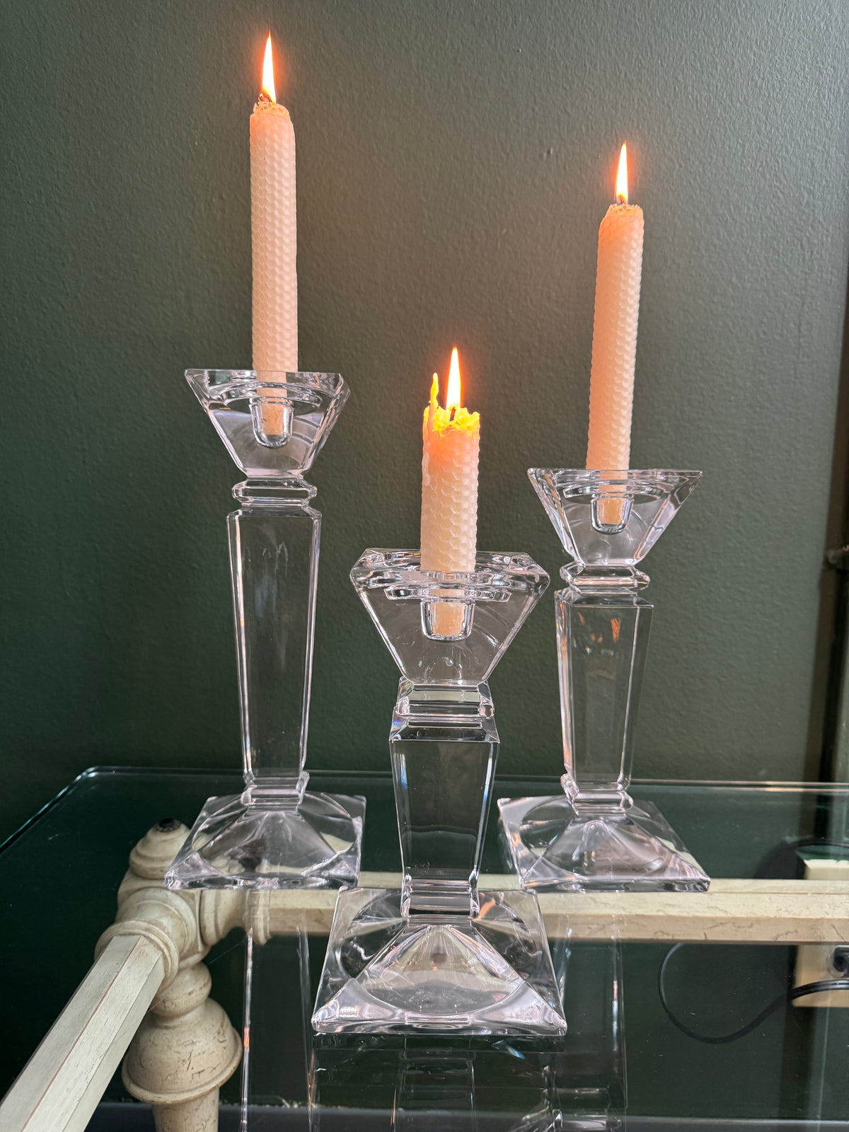 Three clear crystal taper candlesticks with square pyramid bases on a glass table